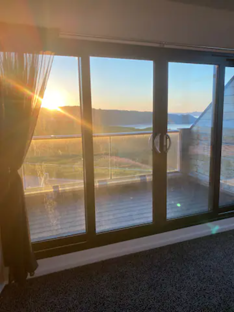 Sun setting over the hills and bay, seen through floor-to-ceiling glass doors at Castle Sunset on the Beach