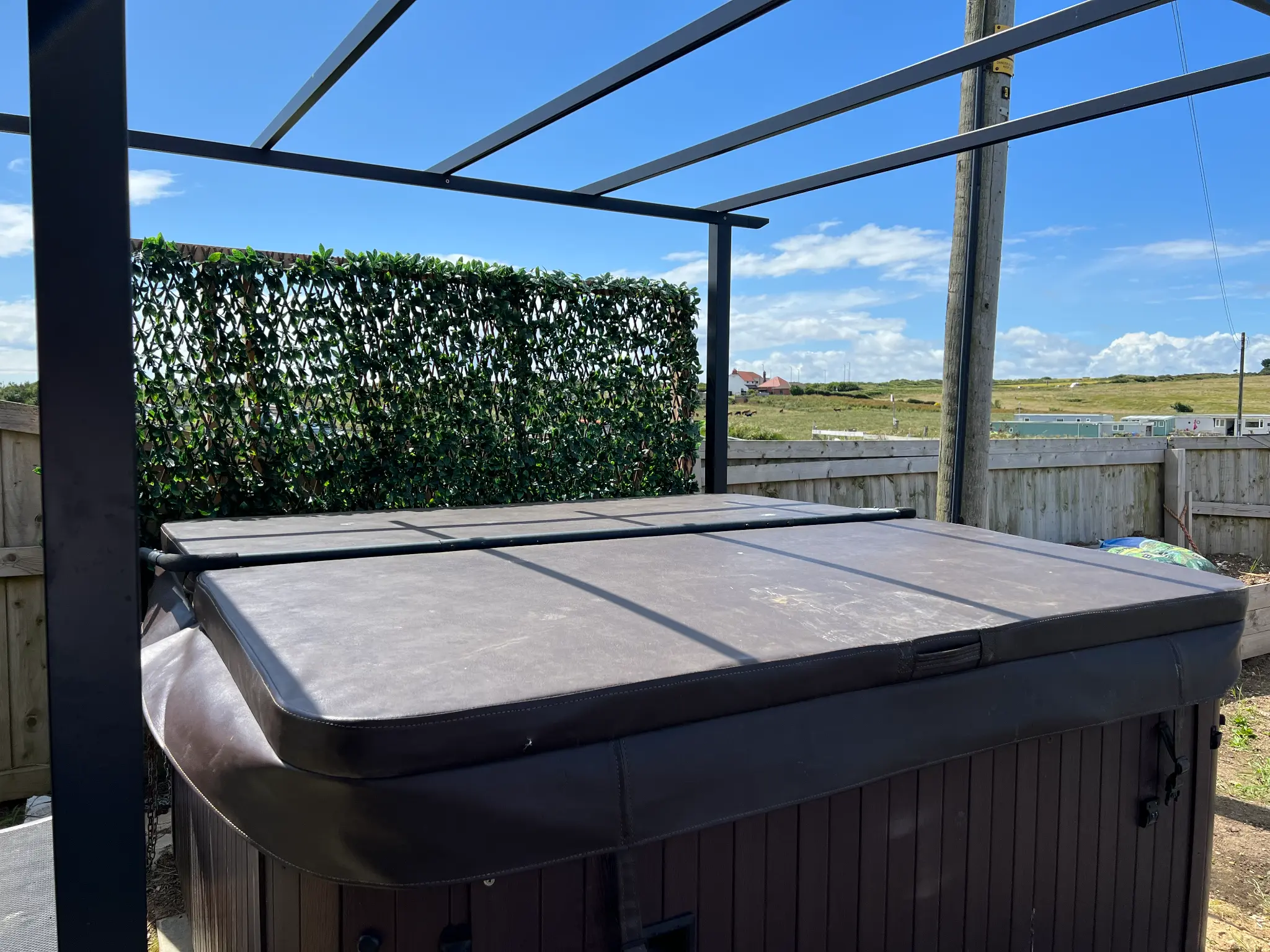 Covered hot tub under a pergola in the enclosed garden at Castle Sunset, with a green screen for privacy
