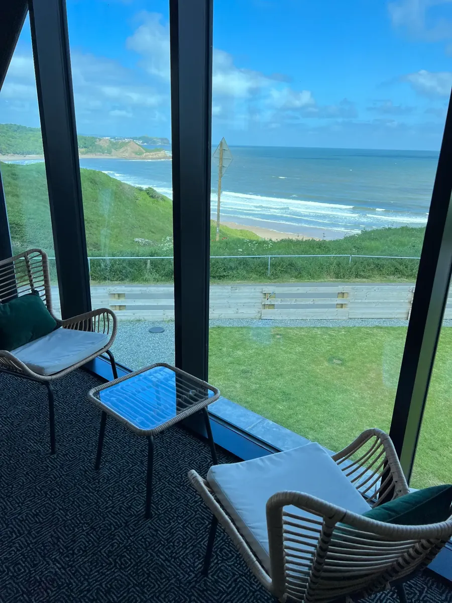 Two chairs at the bedroom's glass wall, with the surf beach of Cayton Bay just below